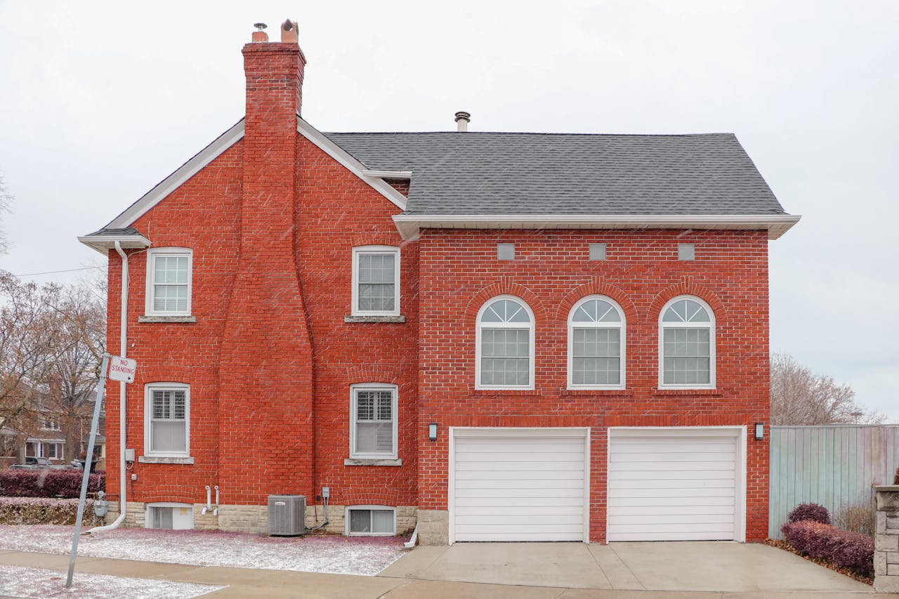 services-03 Red brick house exterior in Toronto with arched windows, chimney, and double garage.